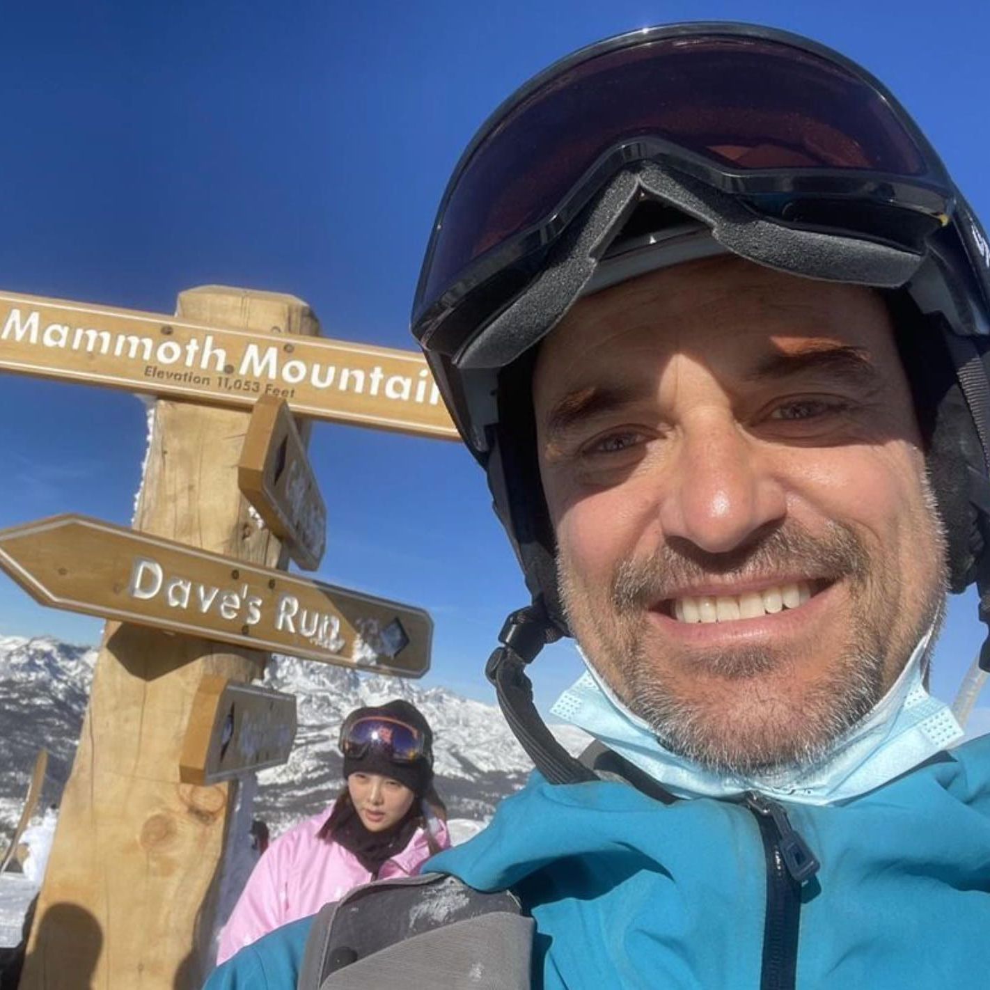 Ryan Levis wearing a ski helmet and goggles stands in front of a sign that says mammoth mountain