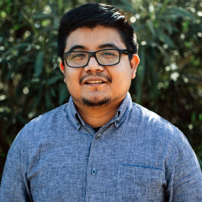Mario Arellanes of Ryan Levis Architect, Inc., wearing glasses and a blue shirt is standing in front of a tree.