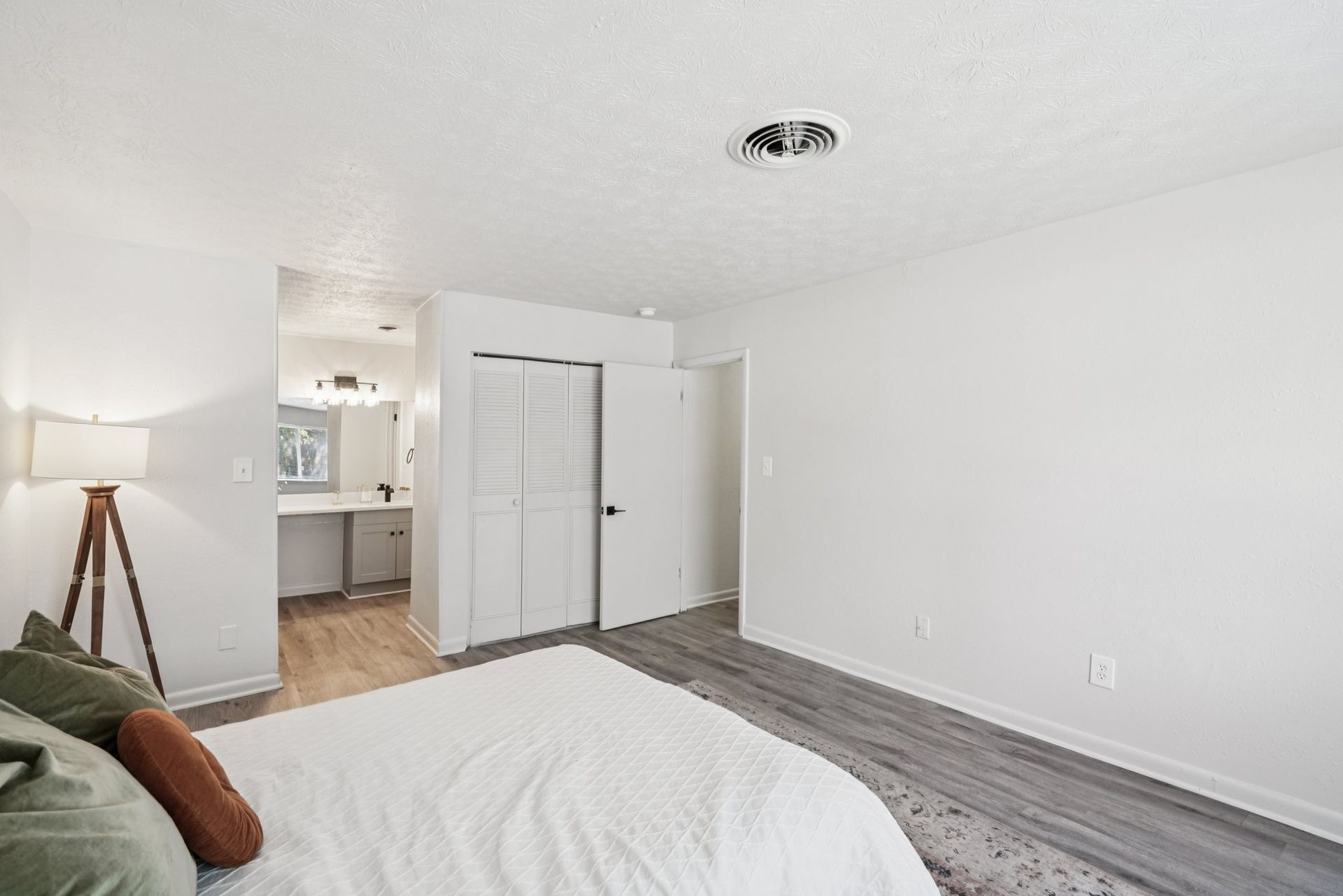 Bedroom with white walls, a bed, a wooden lamp, and an open doorway to a bathroom.