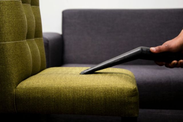 Hand holding a tablet above a green chair beside a gray couch
