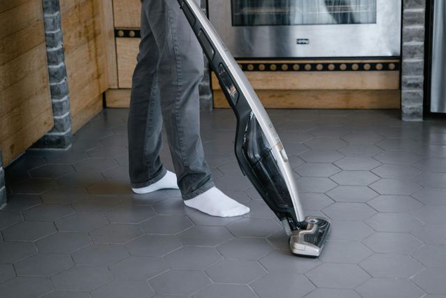 Person vacuuming a tiled floor with a canister vacuum indoors