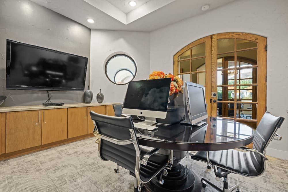 A conference room with a table, chairs, computers, and a flat-screen tv at Marquis at the Reserve in Katy, TX.