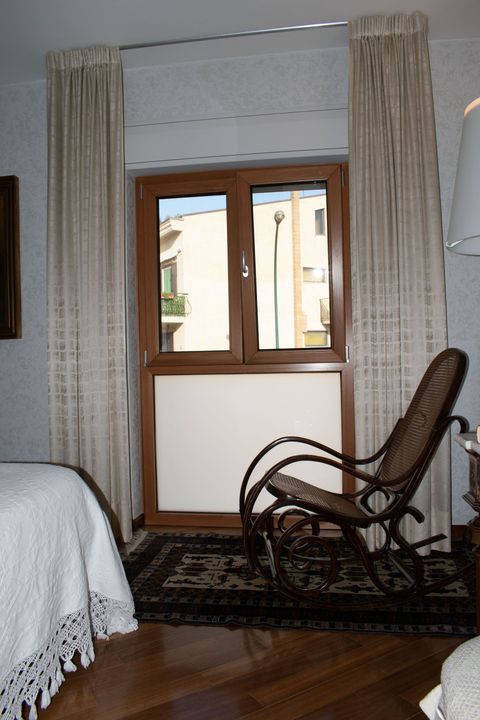 Una porta a doppio battente in vetro con cornice marrone conduce a un balcone con pareti color arancione acceso e ombre sul pavimento.