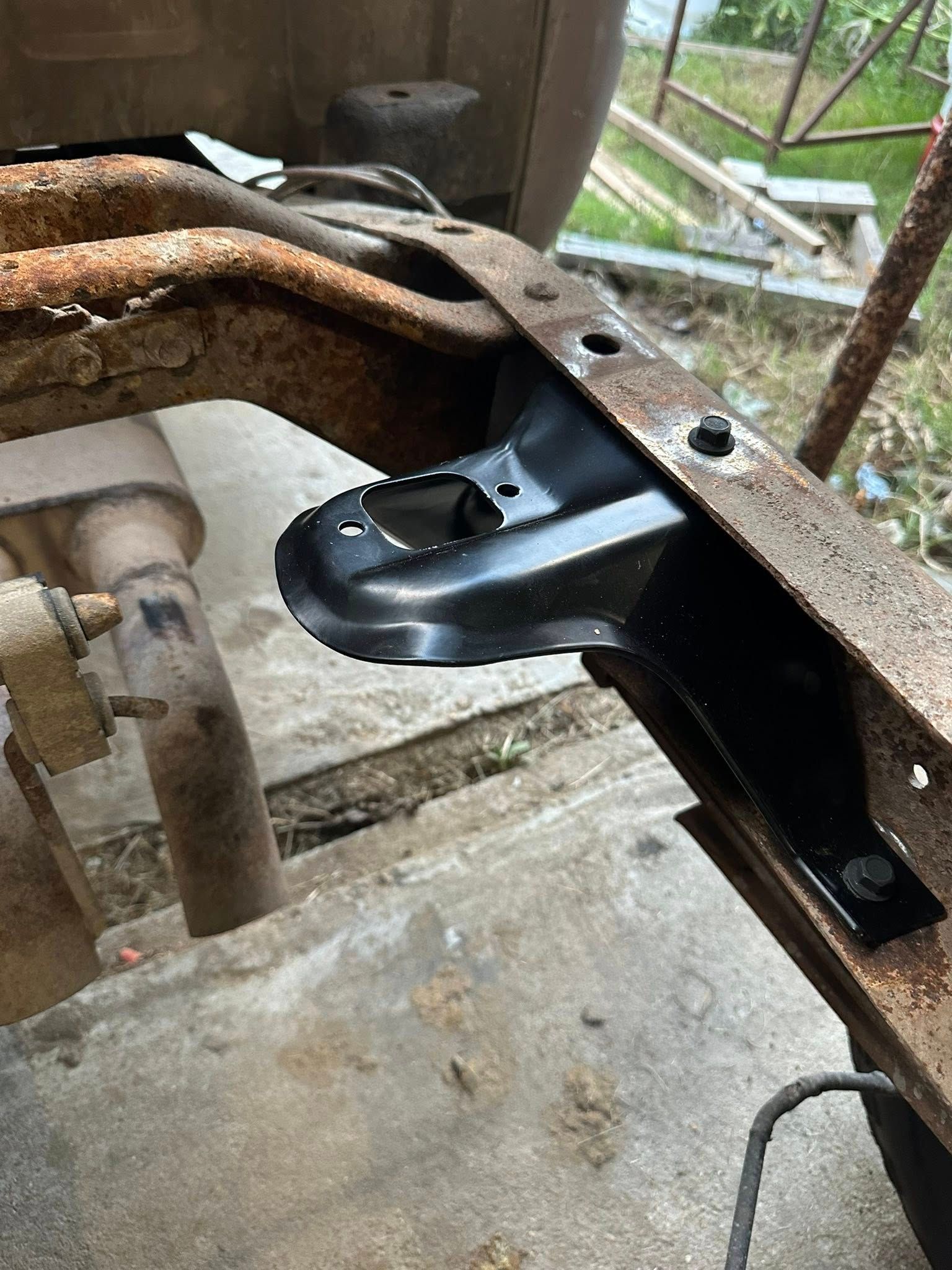 A new black metal shock absorber bracket is installed on a rusted vehicle frame rail.