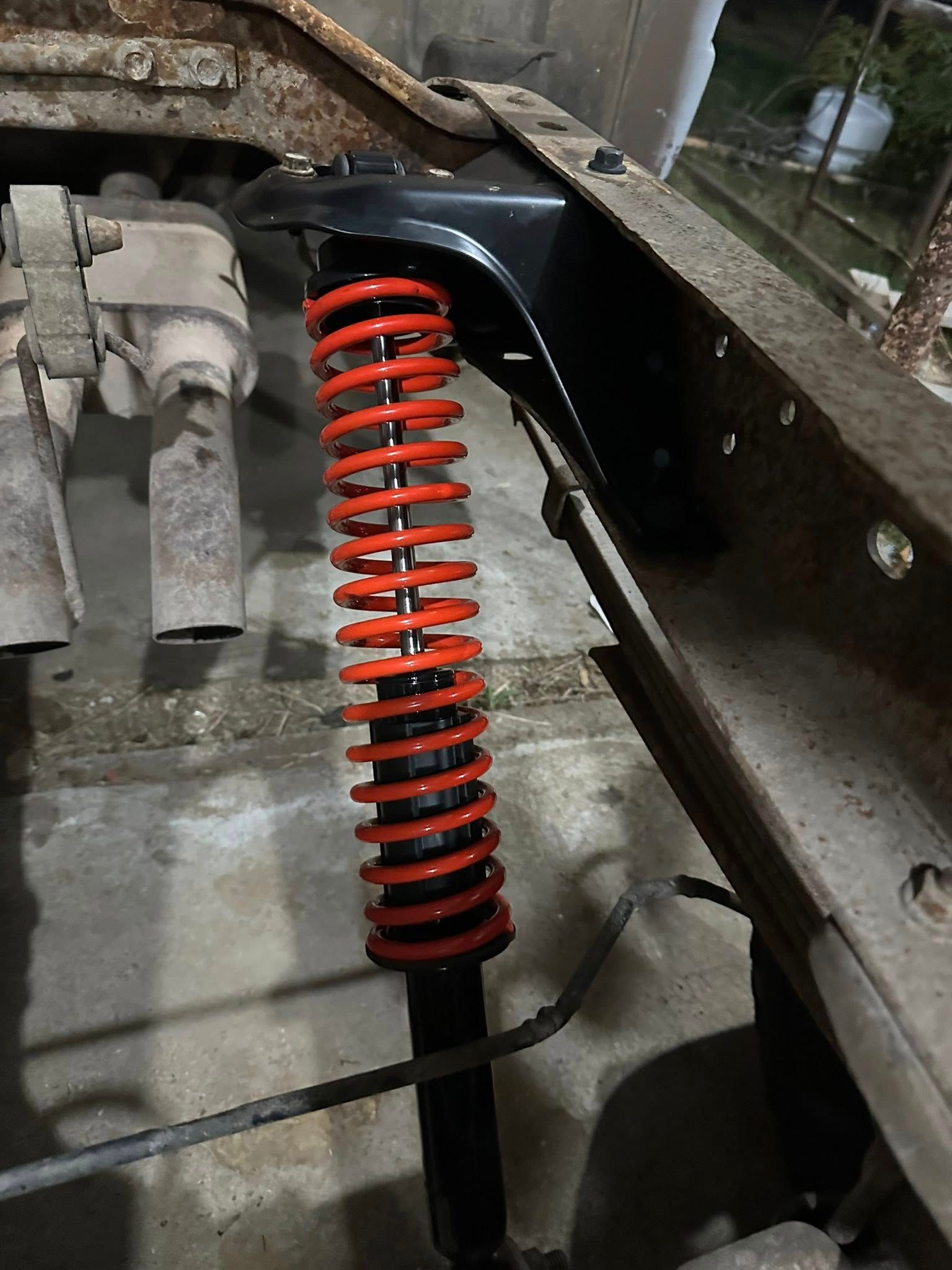 A new red coil-over shock absorber installed on a vehicle chassis frame in a workshop.