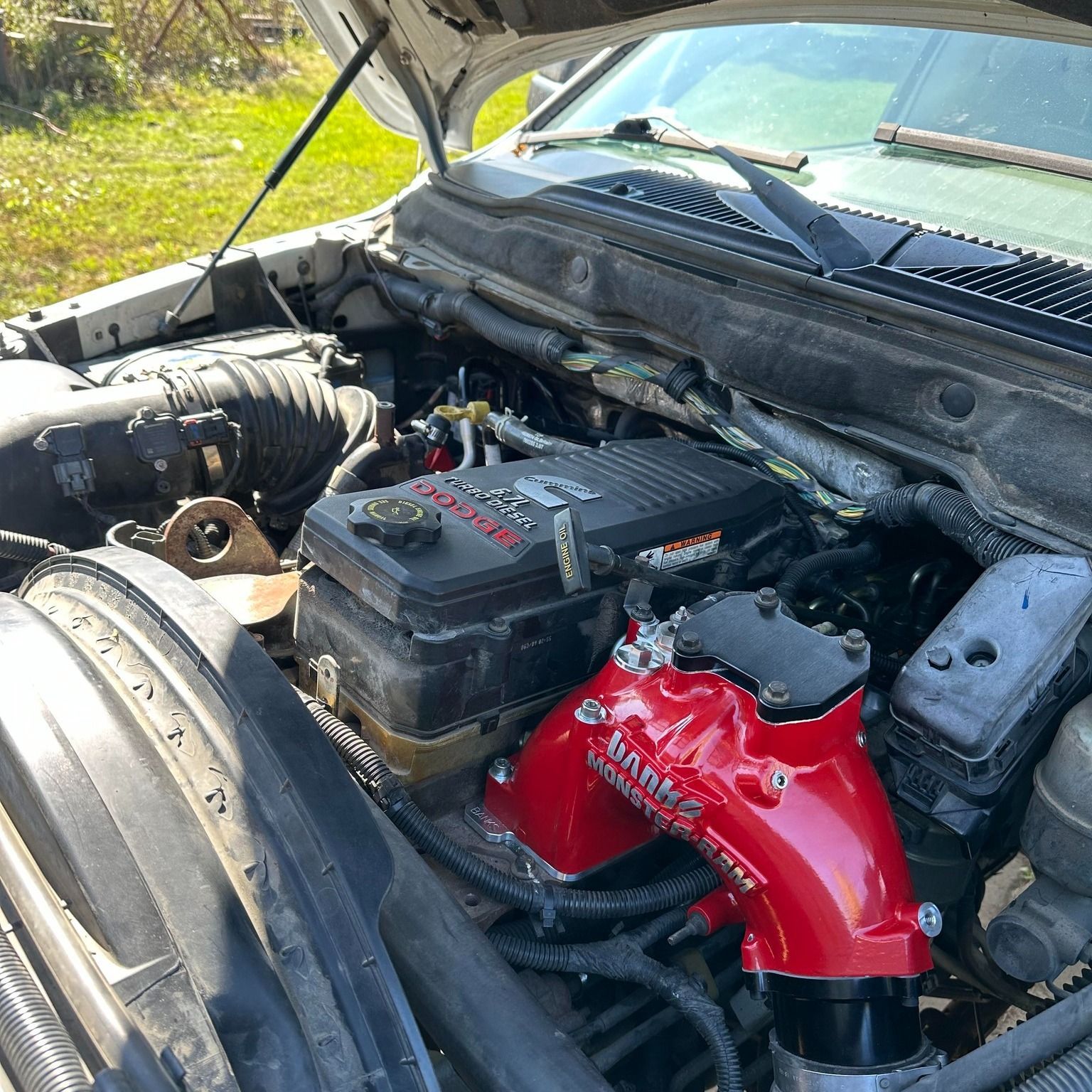 A bright red Banks Power intake manifold is installed on a Cummins diesel engine inside an open truck hood.