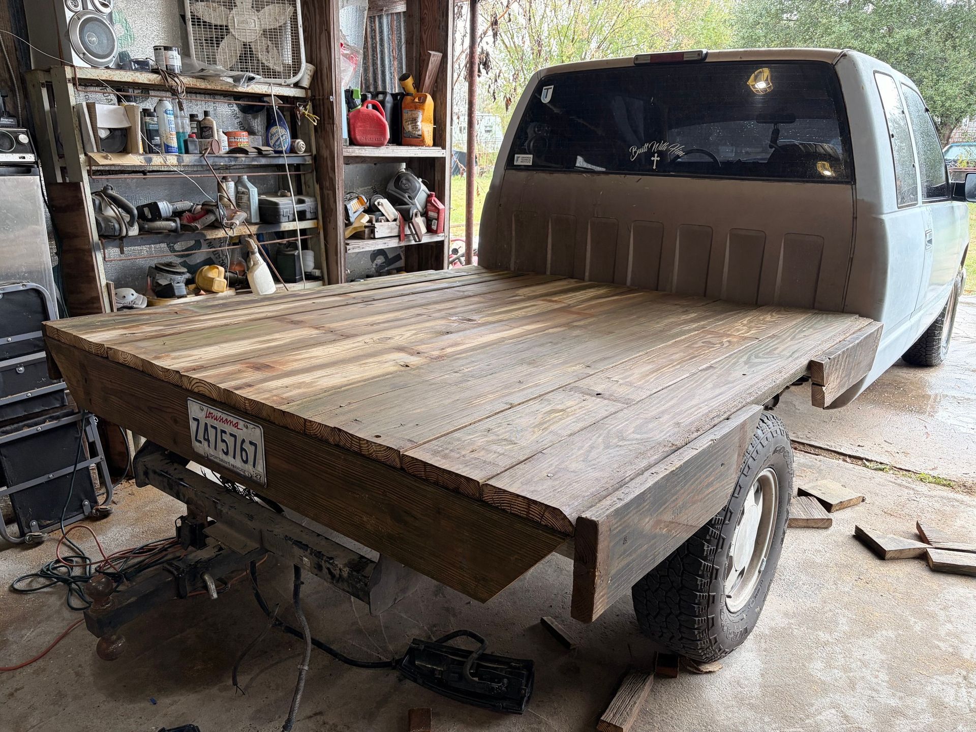 A light-colored pickup truck with a custom flatbed made from weathered wooden planks parked inside a garage.