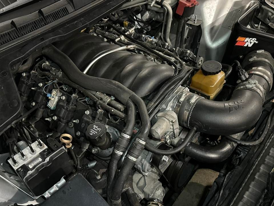 A high-angle view of a clean car engine bay featuring a black intake manifold and a K&N air intake system.