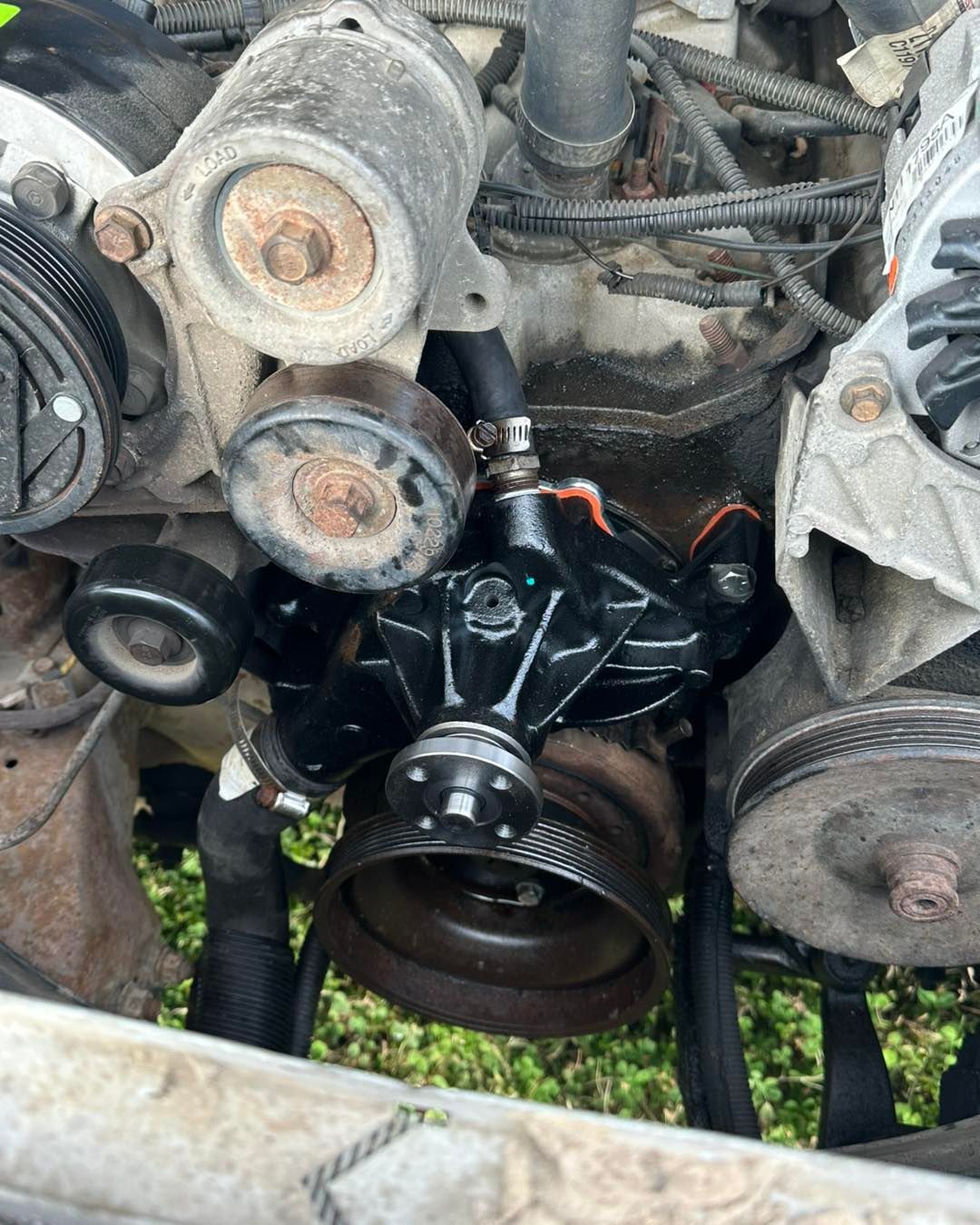 A close-up view of an engine bay featuring a newly installed black water pump, surrounded by pulleys and metal components.