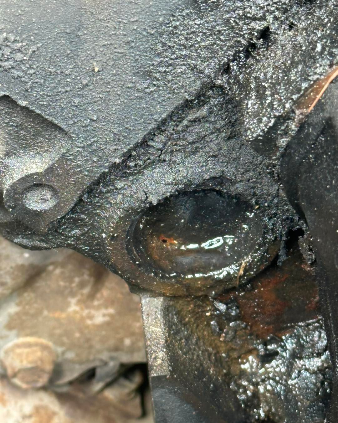 Close-up of a corroded, oil-caked freeze plug on an engine block, with signs of a coolant or oil leak.