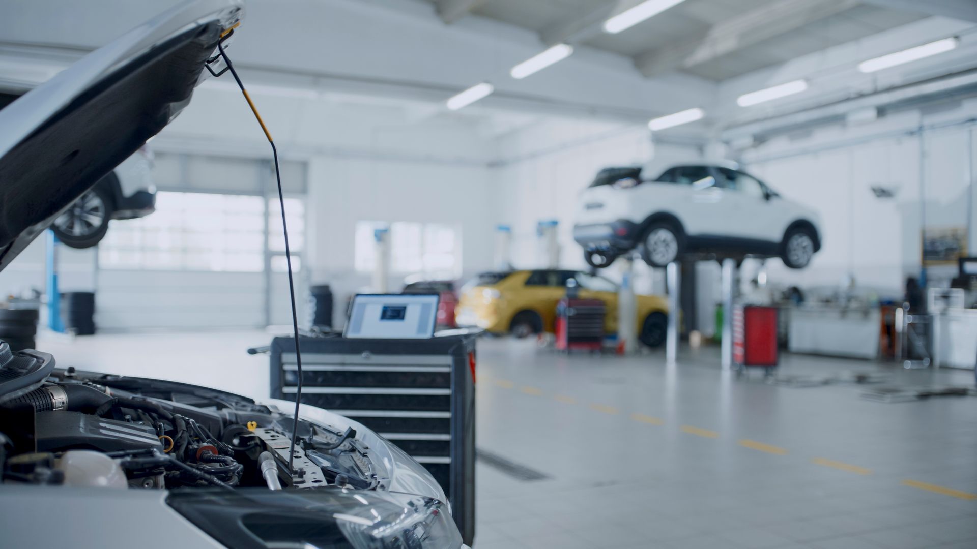 A car is being repaired in a garage with the hood open.