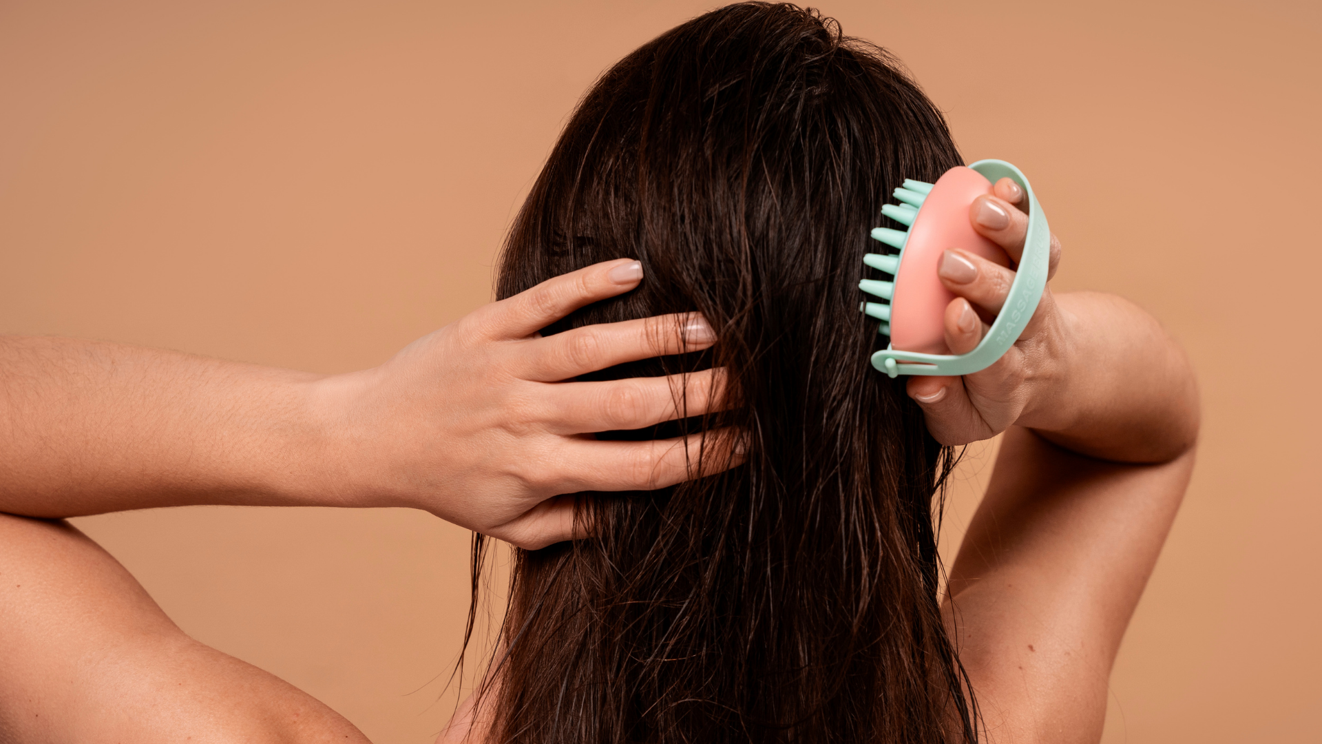 Hands holding wet hair and a turquoise comb against a peach background.