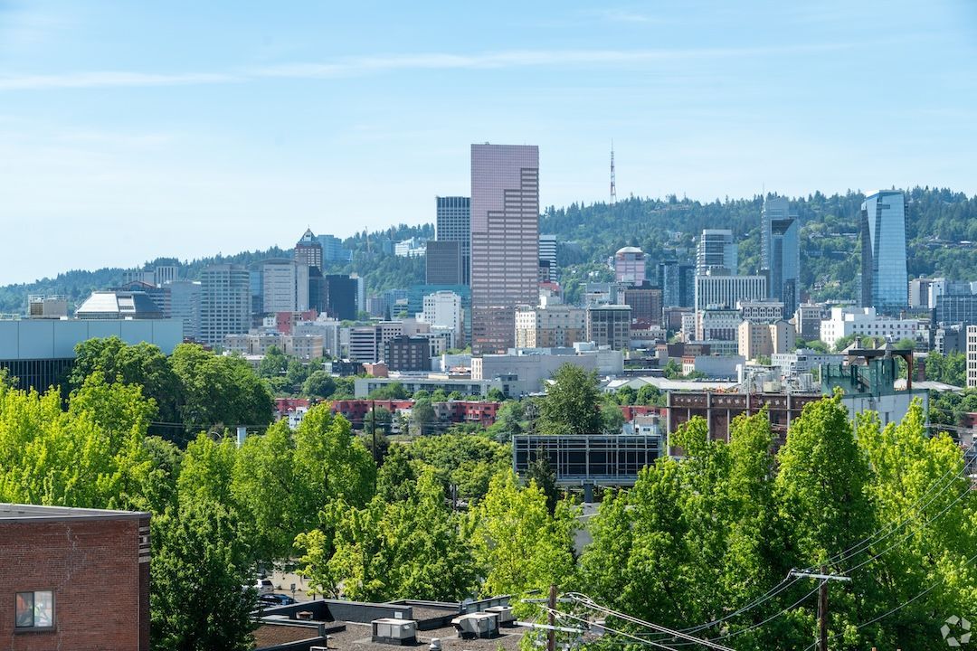 City skyline with a tall pink tower above green trees under a clear blue sky