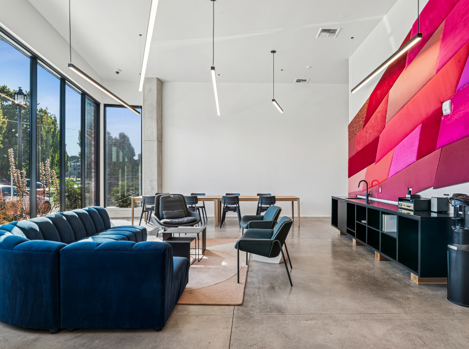 Modern lounge area with blue sofa, large windows, and a colorful geometric wall.