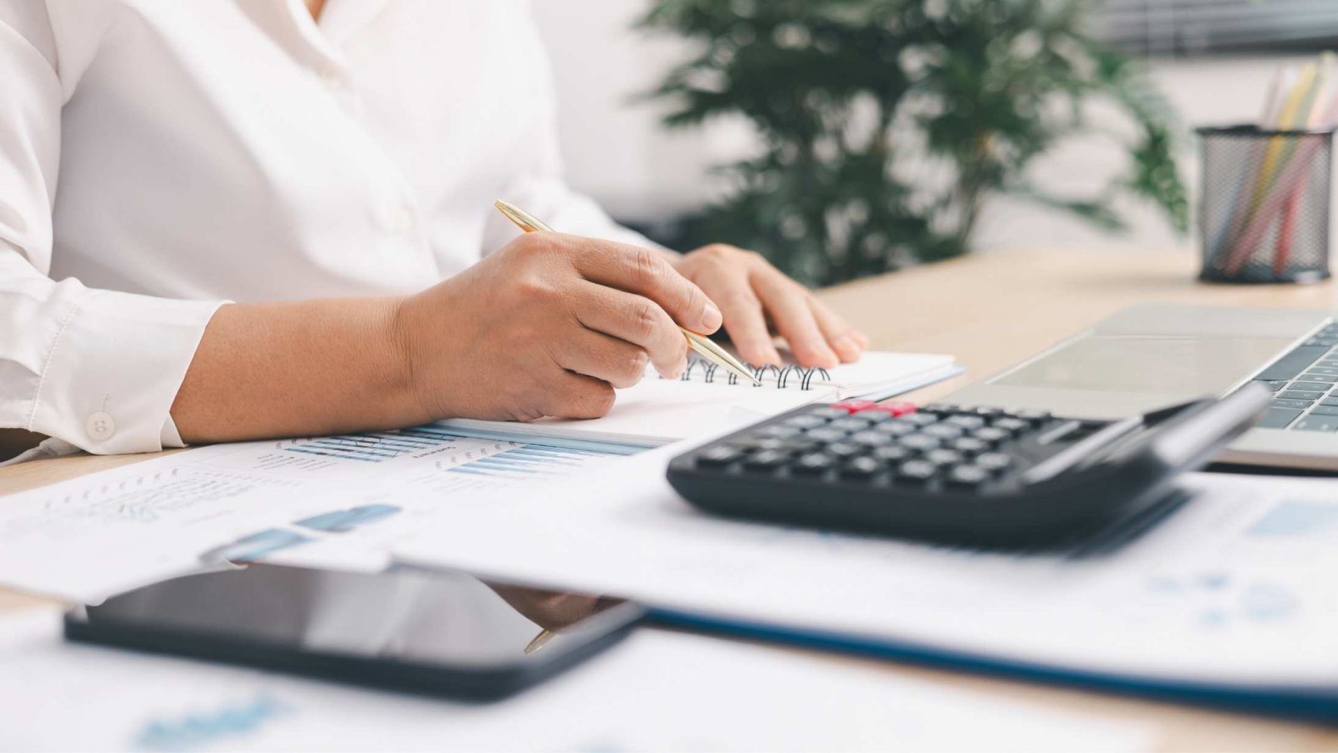 someone at a desk using a calculator while they write on some documents