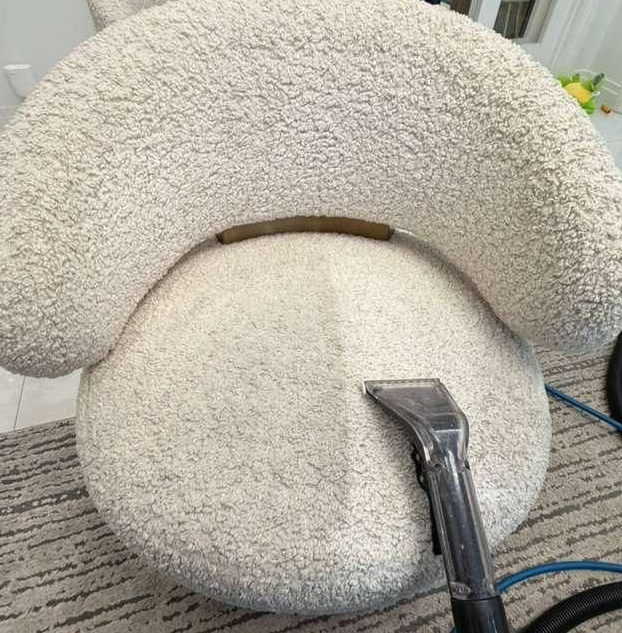 Handheld upholstery cleaner cleaning a beige car seat with gray fabric upholstery