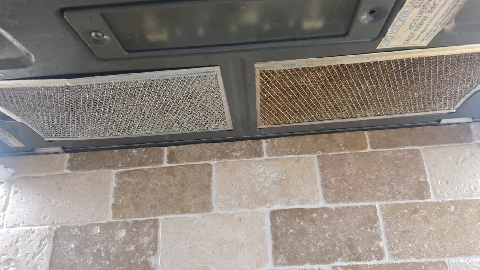 Two rectangular floor vents beneath a fireplace on a beige tiled hearth.