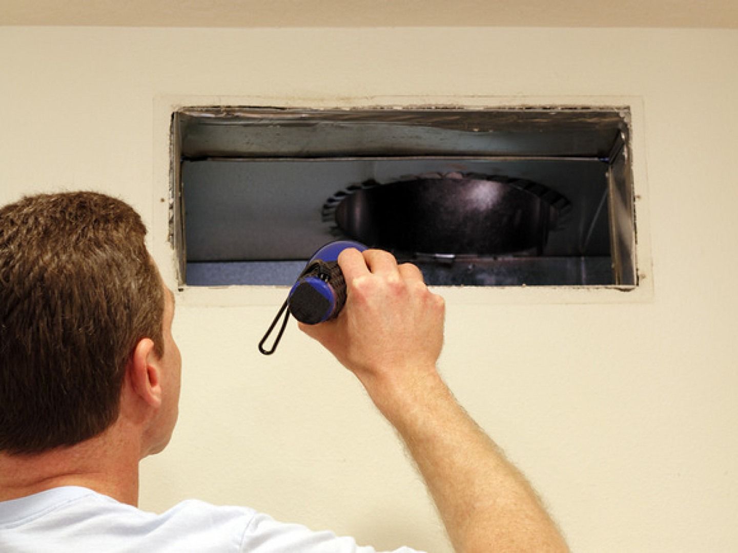 Man inspects air duct with flashlight.