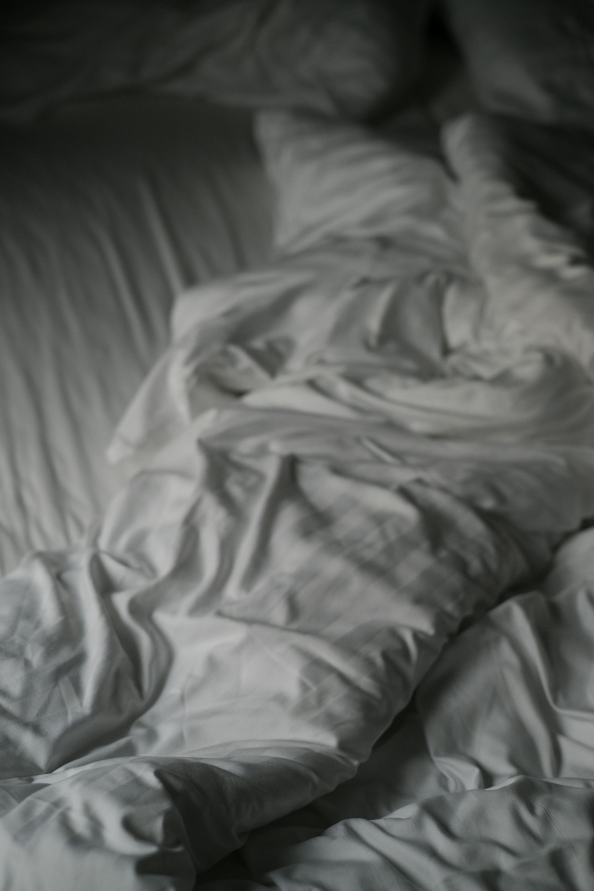 Person sleeping under white sheets on a bed in dim light