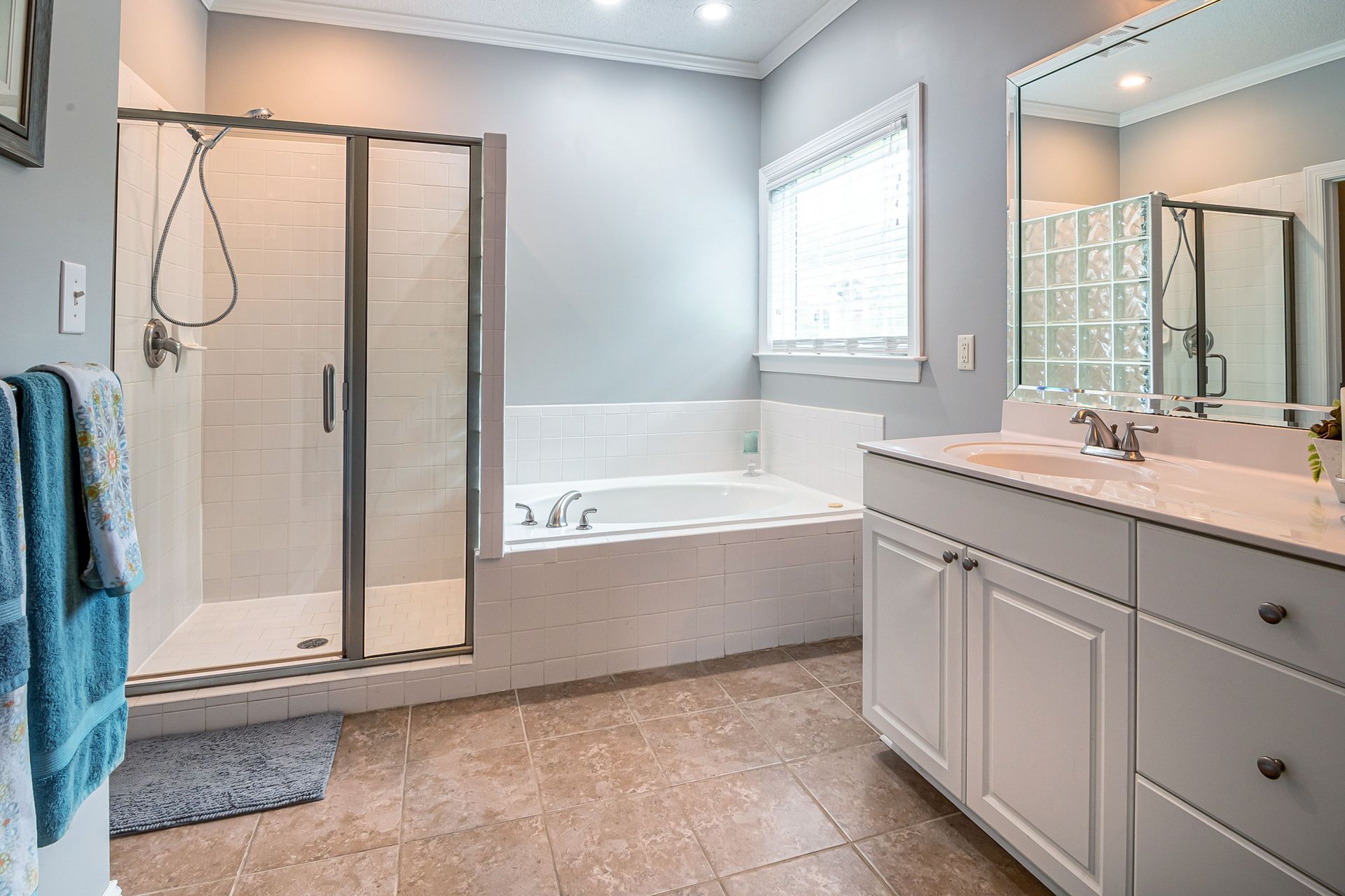 Bathroom with tan tile, wooden vanity, and a window showing a blue sky.
