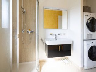 Bathroom with shower, vanity, and stacked washer/dryer; beige and white tones with yellow accent wall.