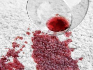 Red liquid spilling from a glass onto a light-colored carpet.