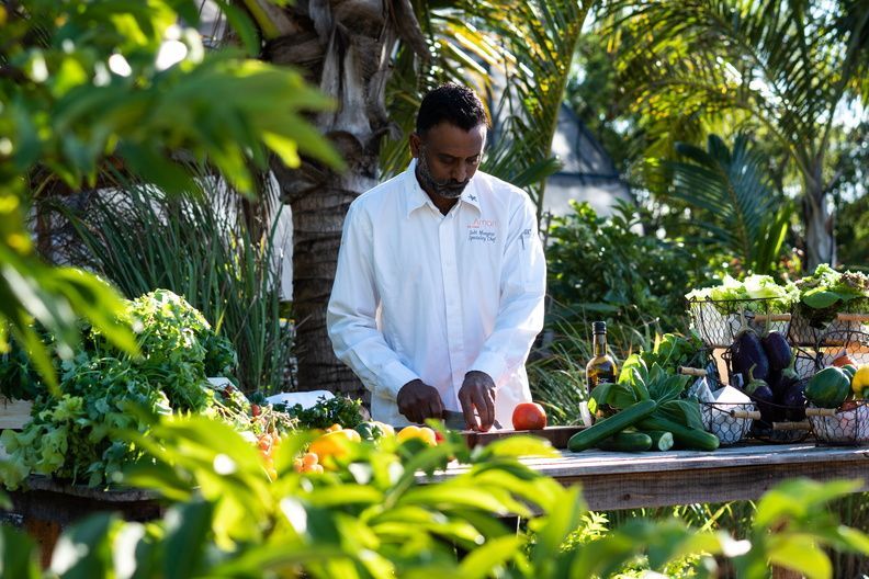 Chef in a white jacket preparing food outdoors amid lush tropical greenery