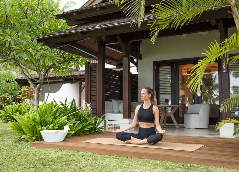 Woman meditating on a porch outside a tropical villa, surrounded by lush greenery