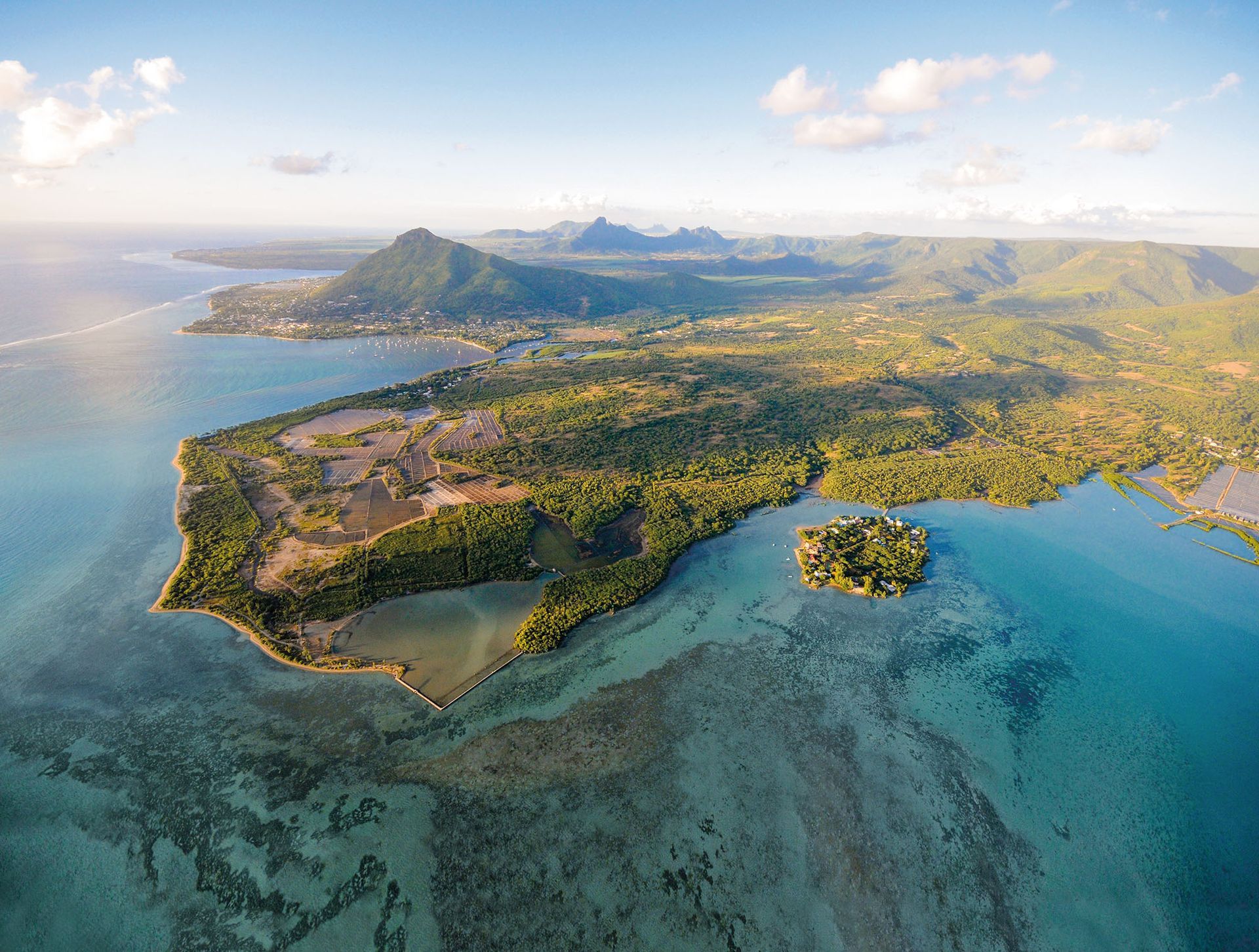Aerial view of a lush tropical island with turquoise waters, coastal hills, and coral reefs.