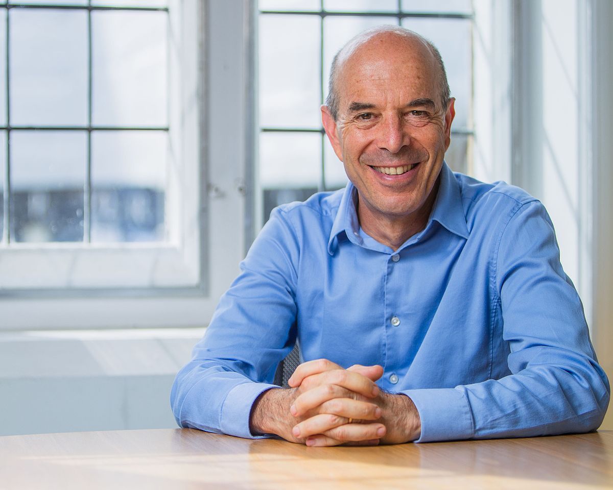 Smiling man in a blue shirt seated at a table in a bright office