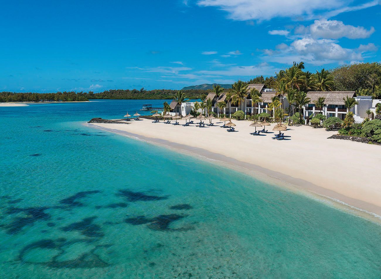 Tropical beach with turquoise water, white sand, palm trees, and resort loungers under a blue sky