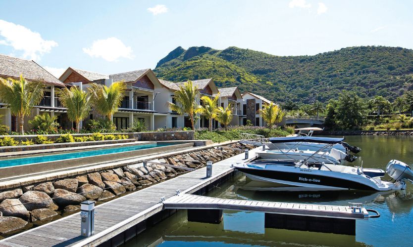 Luxury waterfront resort with docks, moored boats, and tropical hills in the background
