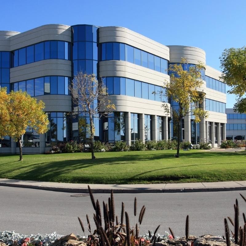 Modern office building with blue glass windows, beige exterior, and green lawn.