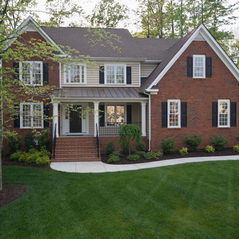 Two-story brick house with tan siding, black shutters, and a green lawn.