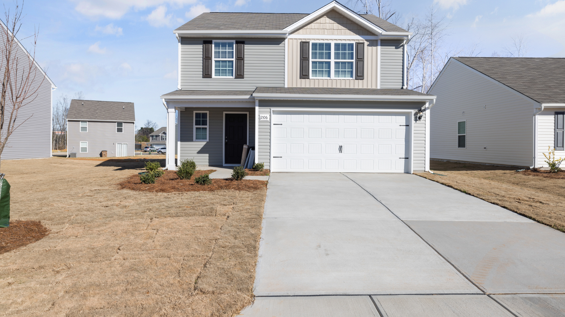 Two-story gray house with a concrete driveway and a two-car garage.  Dry yard.
