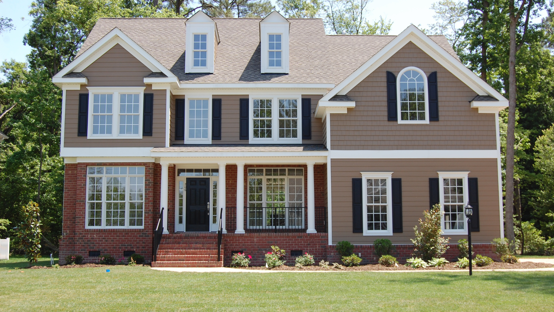 Two-story brown house with brick, white trim, black shutters, and a front lawn.