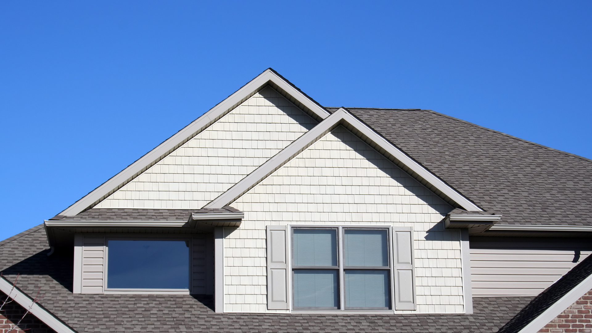 Gabled roof with white siding and two windows against a clear blue sky.