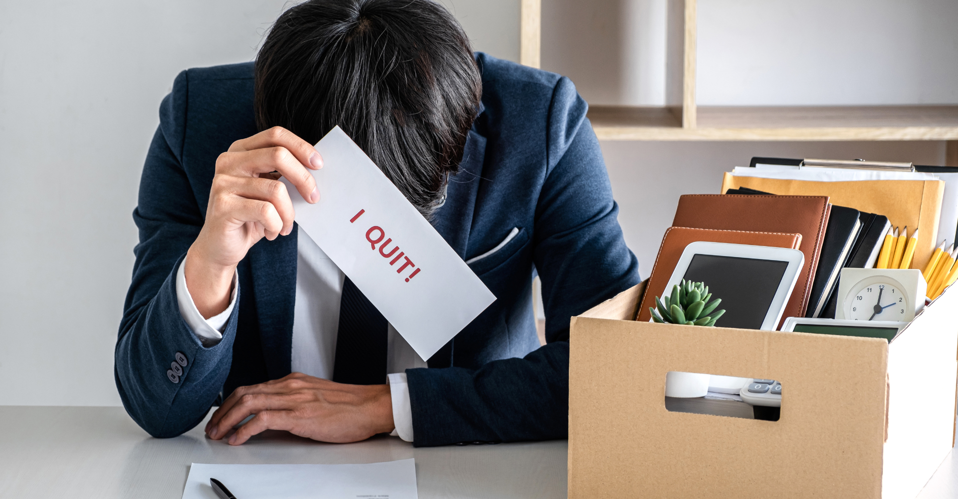 A person at a desk, head down, holding a letter labeled 