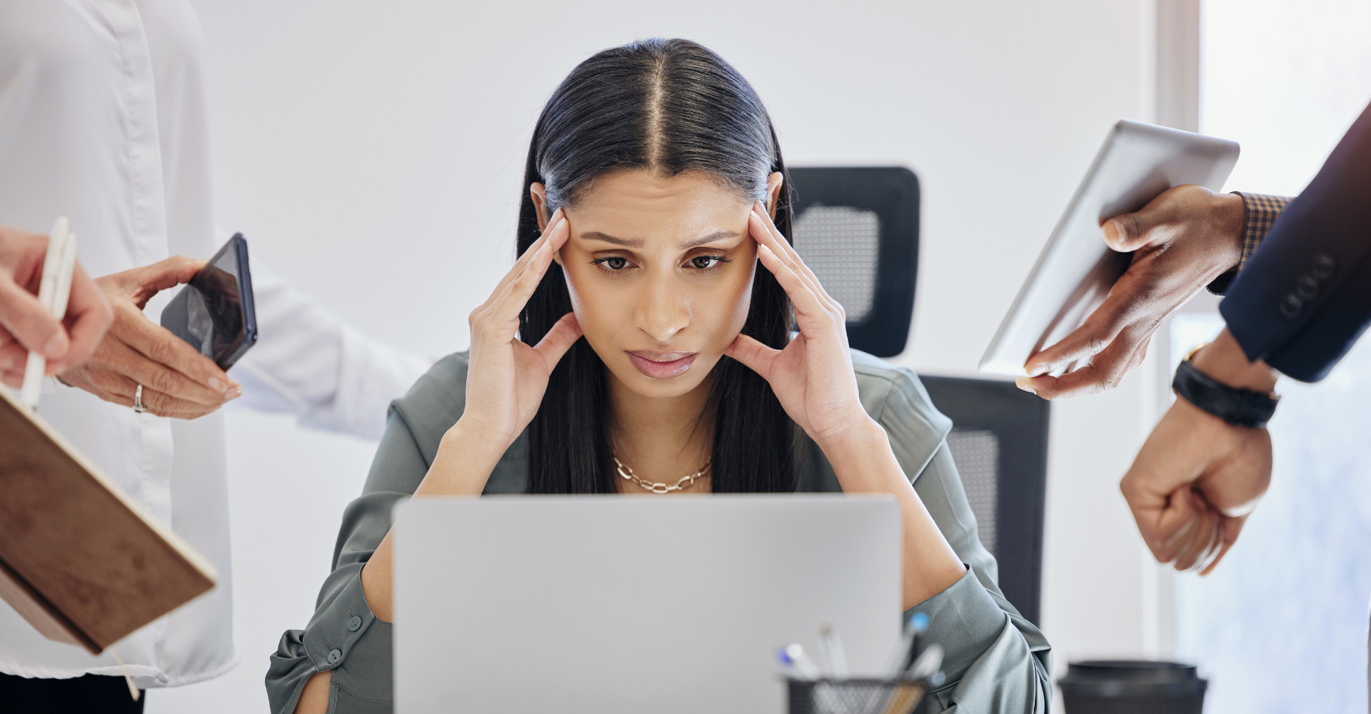 Frustrated woman at a desk with a laptop, holding her temples. Surrounding hands hold phones, a notebook, and a tablet.