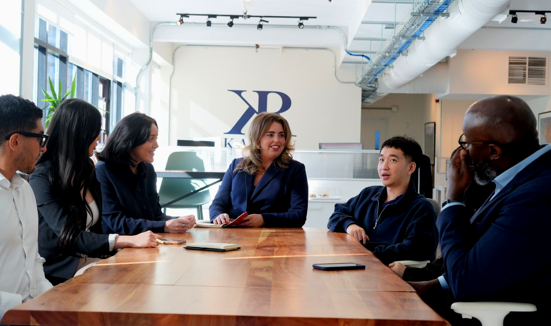 Corporate team seated around a wooden conference table in a modern office meeting room.