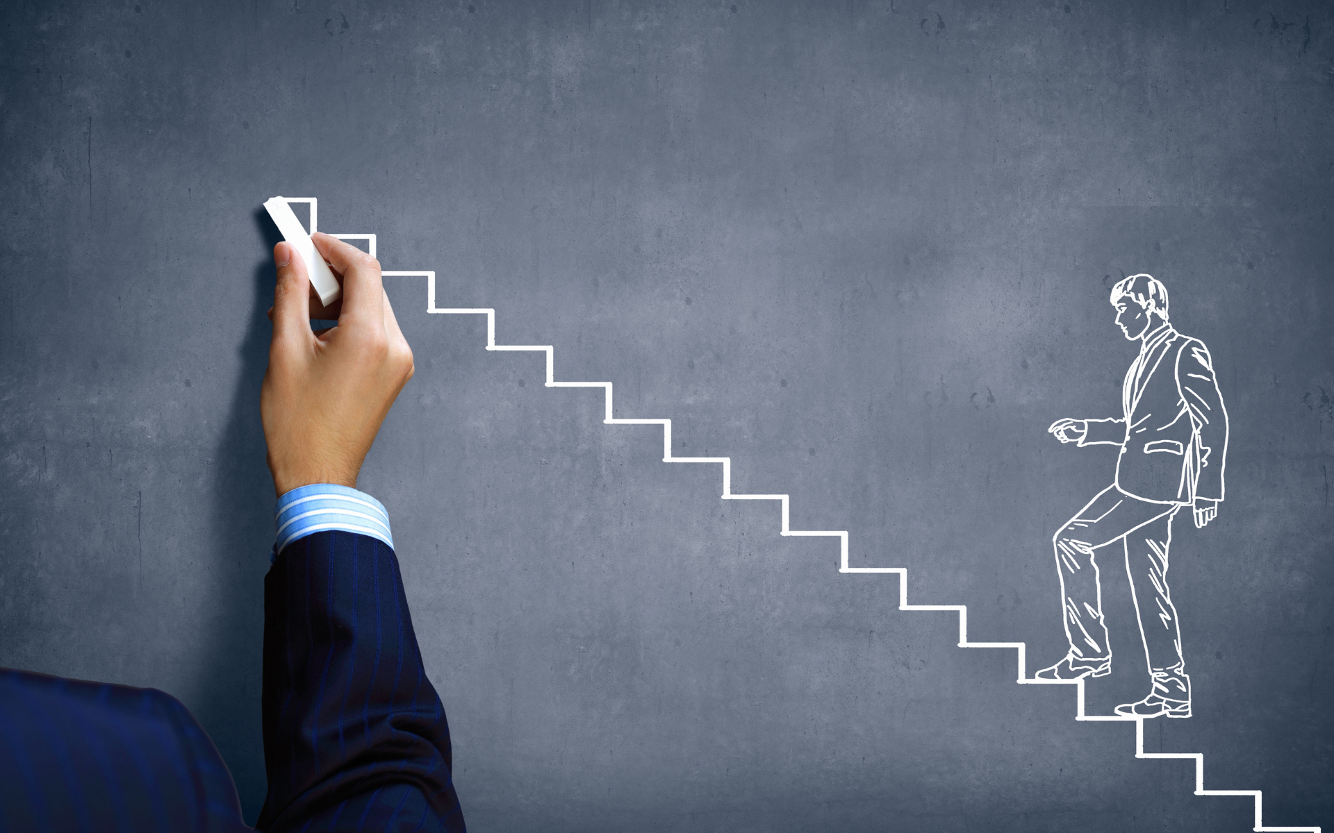 A hand in a suit draws stairs with chalk on a chalkboard. A sketched figure of a man in a suit climbs the steps.