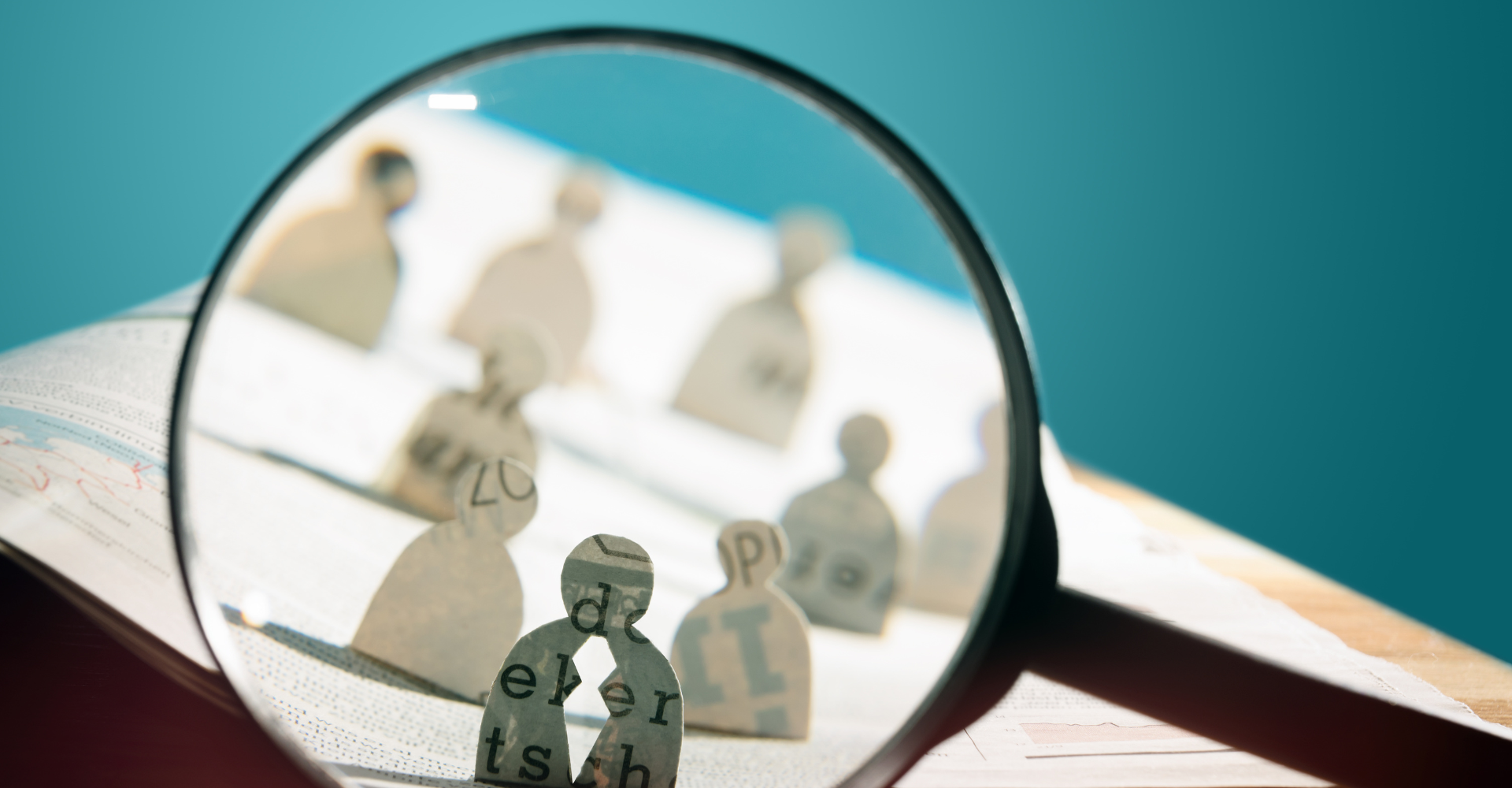 Magnifying glass over paper cutout figures on a printed page, focusing on letters and words.
