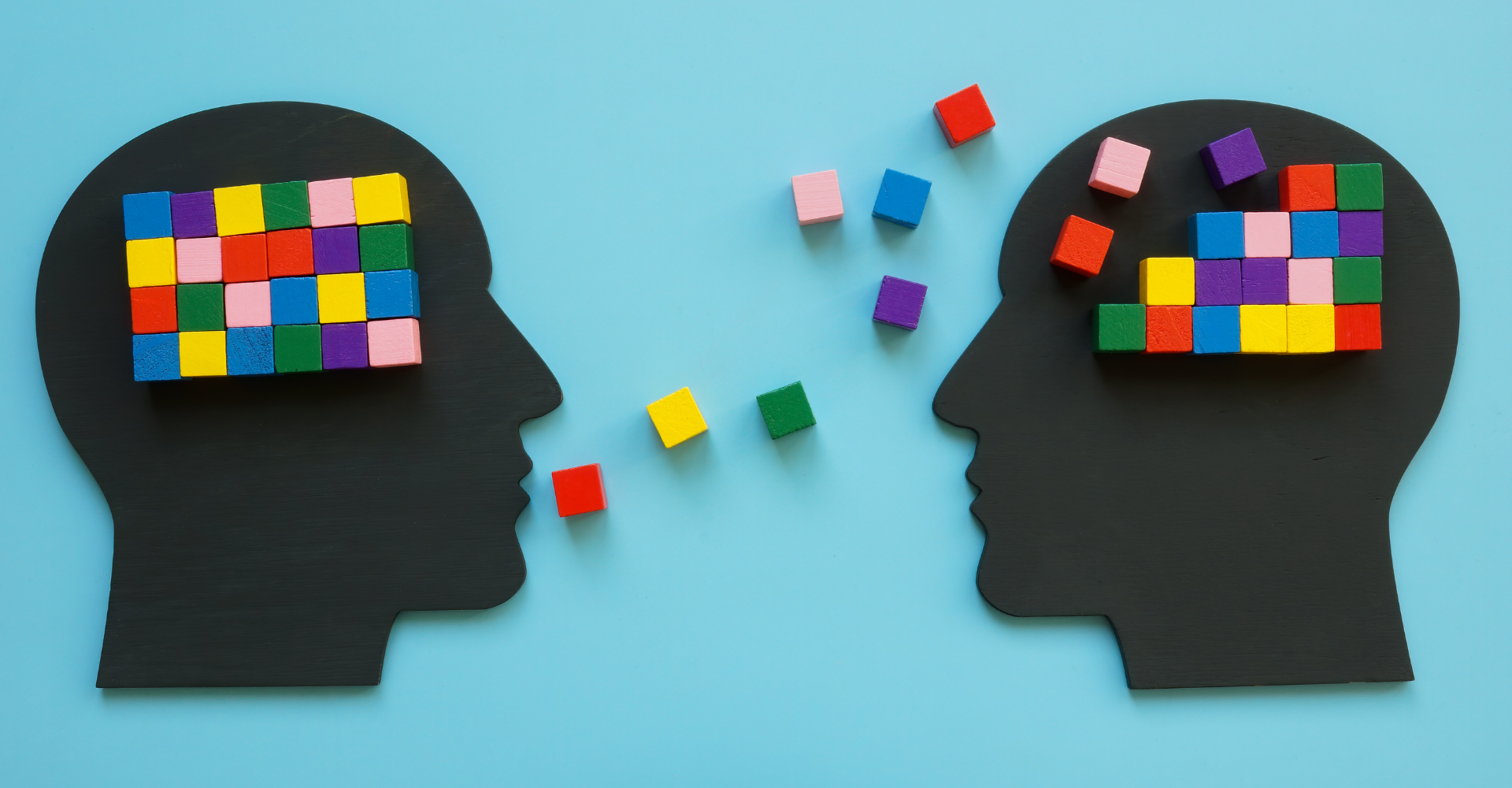 Silhouettes of two heads facing each other, with colorful blocks in and between them, suggesting shared ideas.