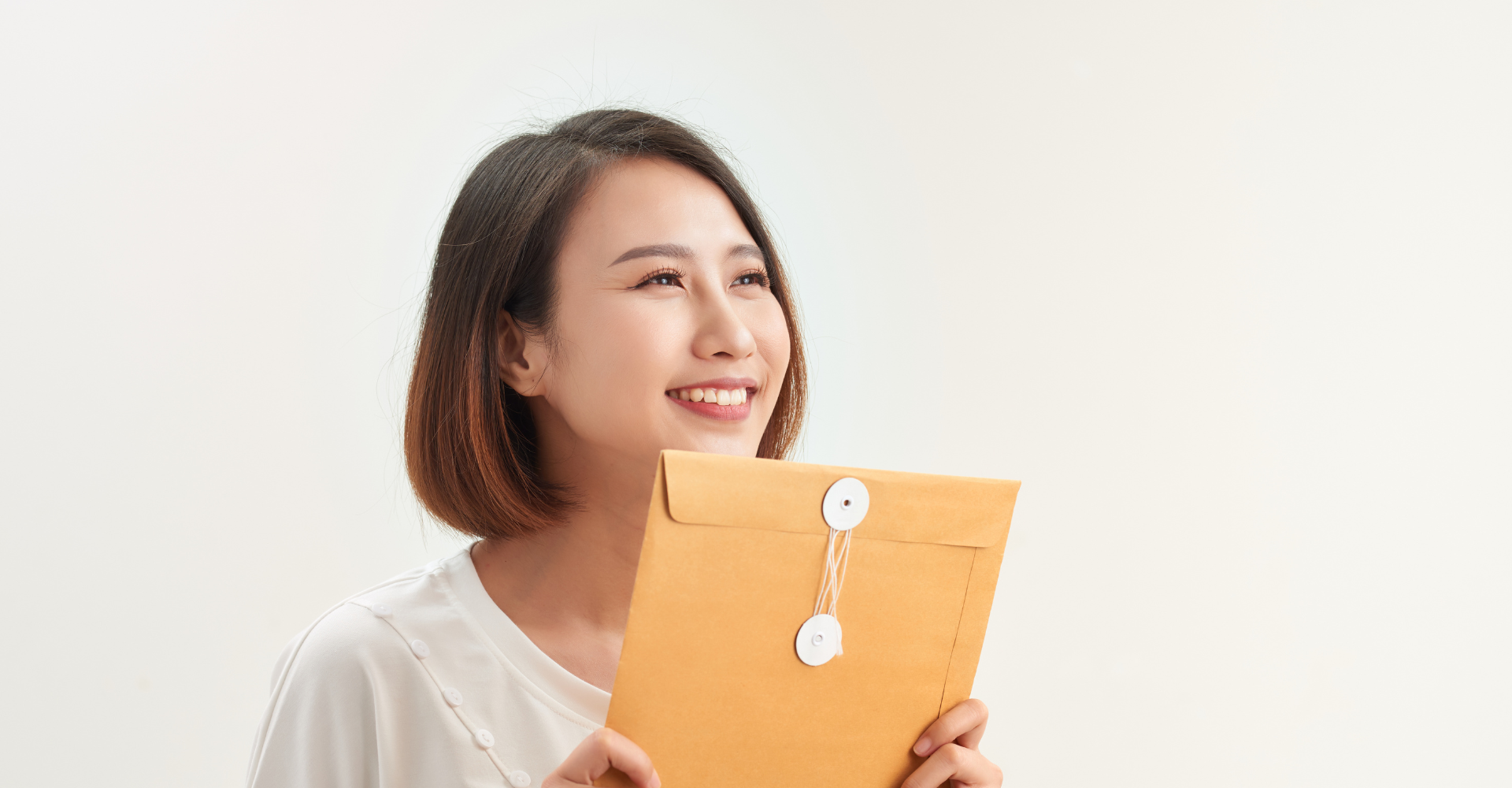 A woman with short brown hair smiles warmly, holding a sealed orange envelope.