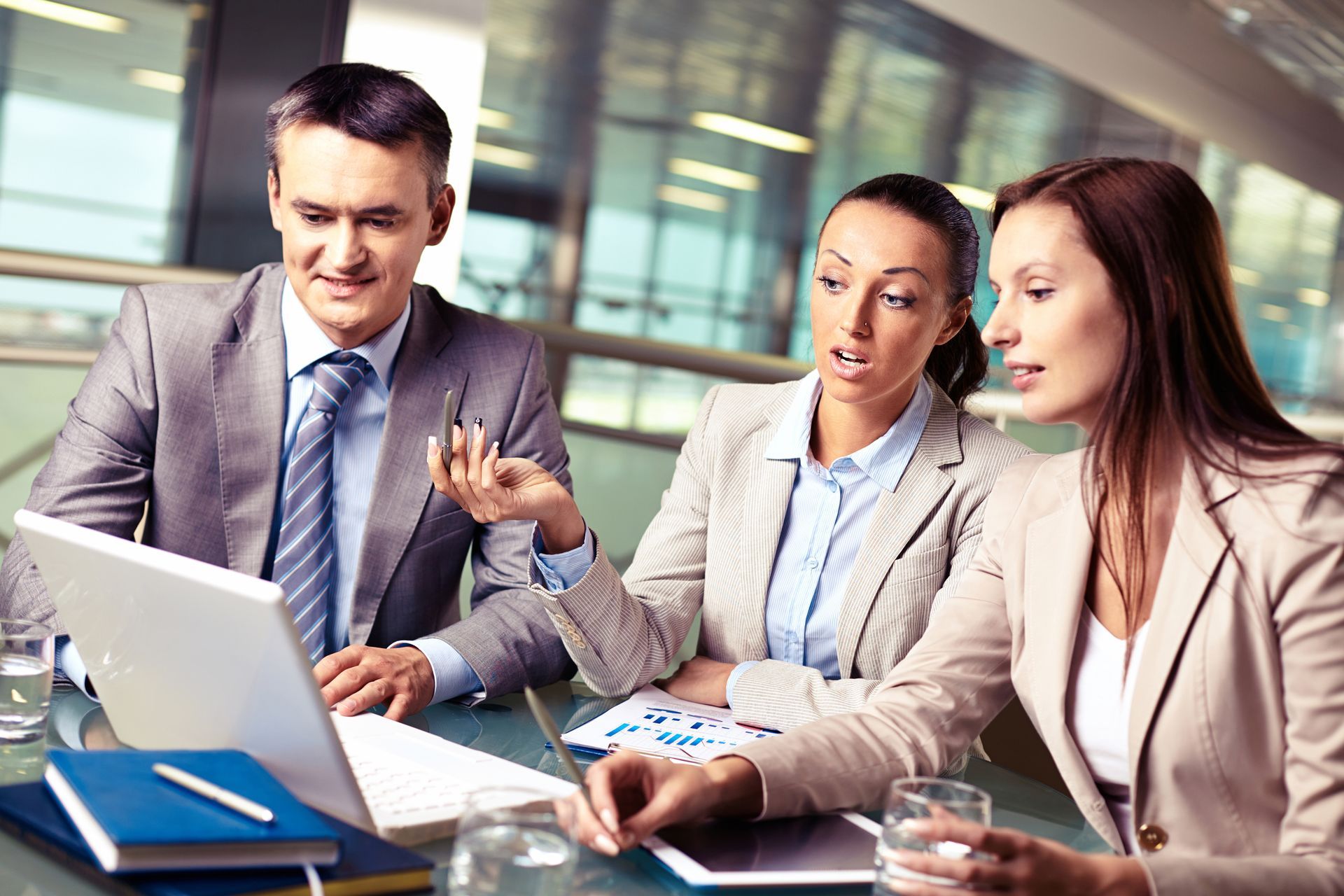 Three business professionals in suits are engaged in a meeting, focused on a laptop screen. They appear collaborative and thoughtful.