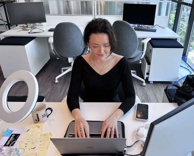 A woman in a black top works on a laptop at a modern office desk.