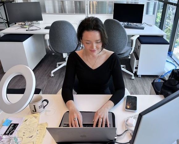 A woman in a black top works on a laptop at a modern office desk.