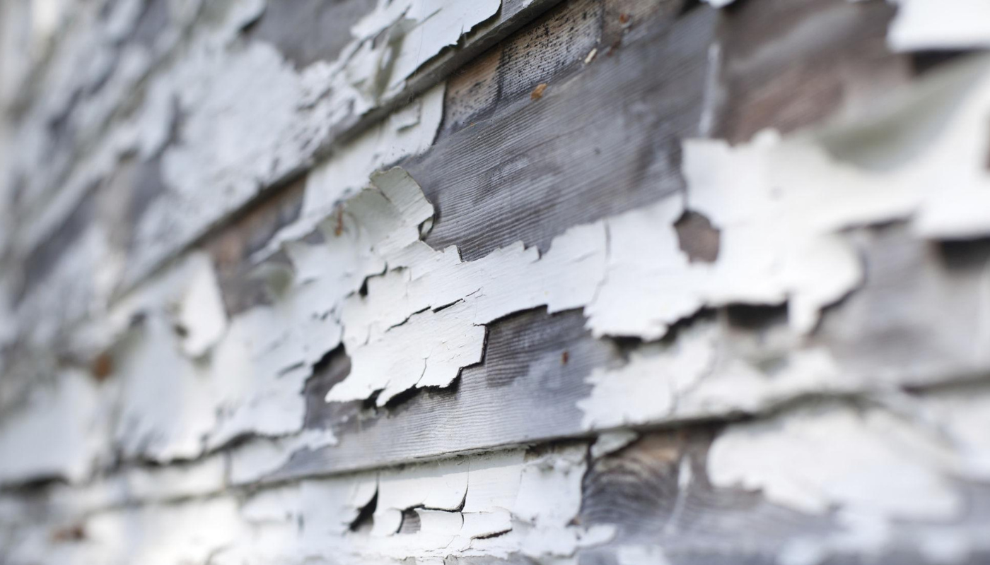 White paint peeling off weathered wooden siding.
