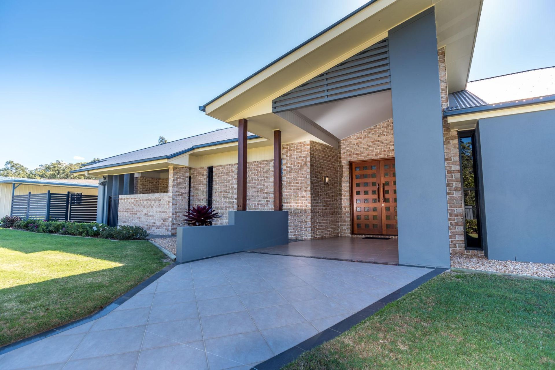 Modern house with gray and tan exterior, wooden door, and a concrete driveway on a sunny day.