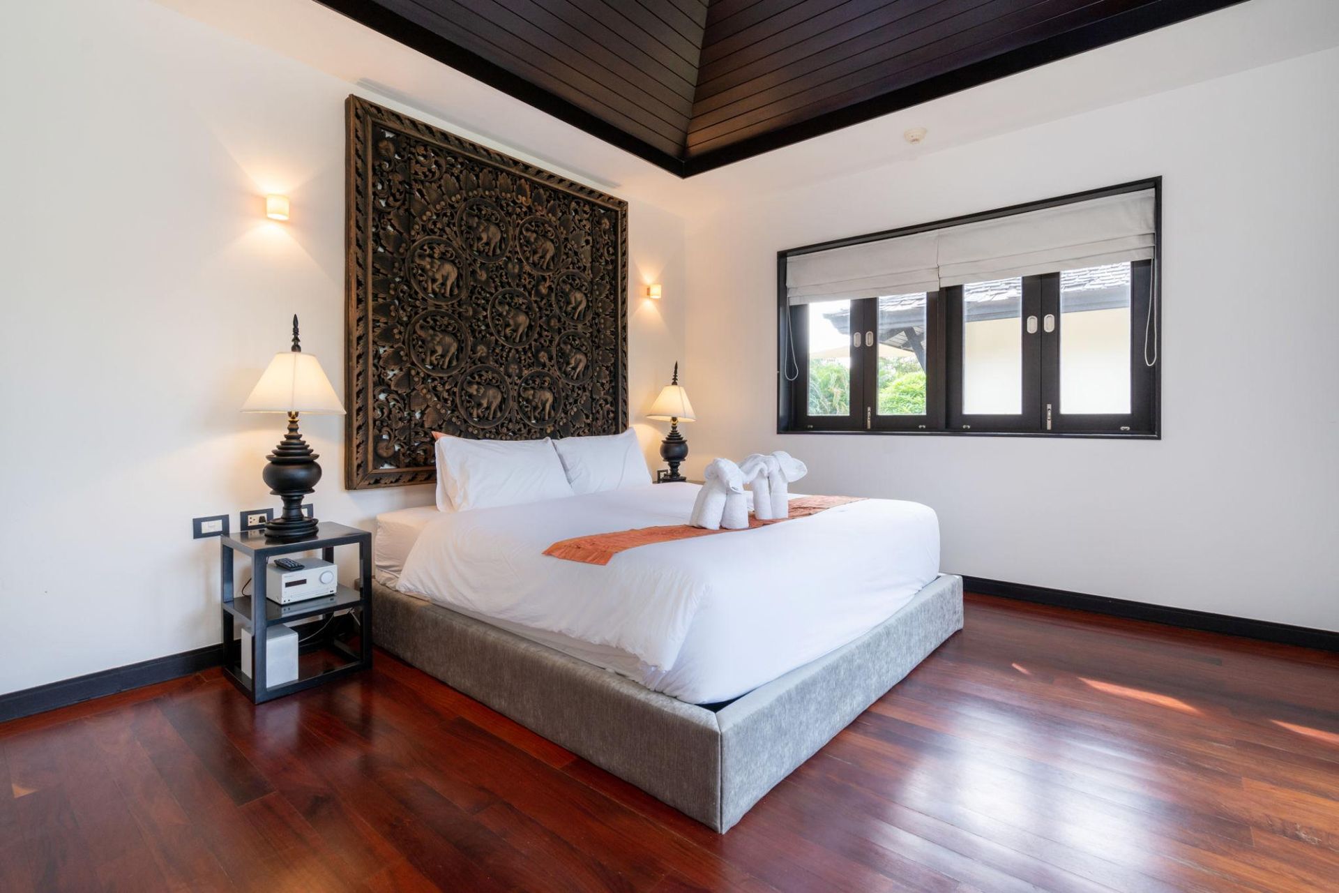 Bedroom with dark wood floors, a bed, and a carved wooden headboard.